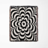 Black and white psychedelic flower woven blanket throw tapestry with fringe vertical full view on a light gray background.