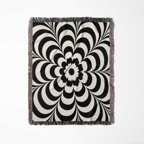 Black and white psychedelic flower woven blanket throw tapestry with fringe vertical full view on a light gray background.