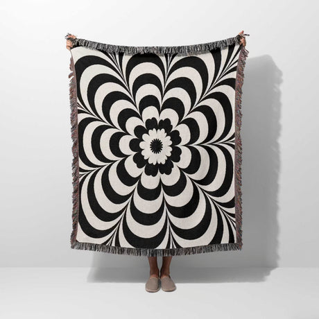Black and white psychedelic flower woven blanket throw tapestry held by a person against a white background.