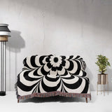Black and white psychedelic flower woven blanket throw tapestry on a sofa against a light gray wall.