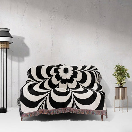Black and white psychedelic flower woven blanket throw tapestry on a sofa against a light gray wall.