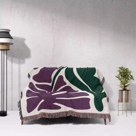 Floral-patterned purple Matisse flowers woven throw blanket draped over a chair against a white wall.