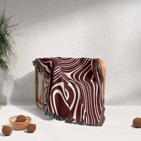 Red abstract woven throw blanket with geometric pattern draped over a wooden chair against a white wall.