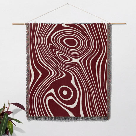 Red abstract woven throw blanket with a swirling pattern in red and white on a wooden rod against a white wall.
