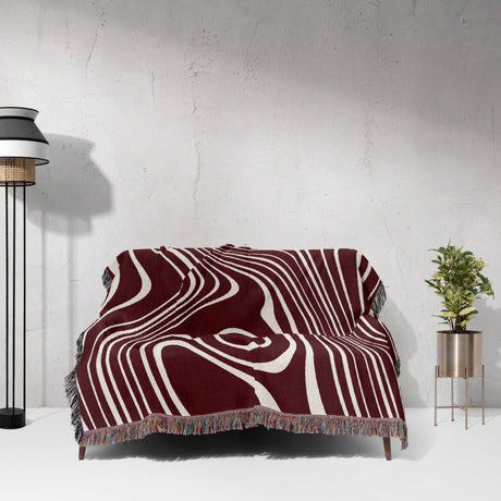 Red abstract woven throw blanket draped over a chair against a light gray wall.