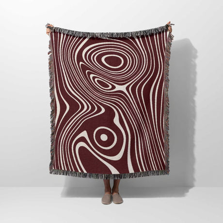 Person holding a patterned red abstract woven throw blanket with concentric circle design on a white background