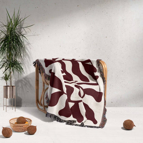 Red leaf Matisse throw blanket draped over a chair against a white wall.
