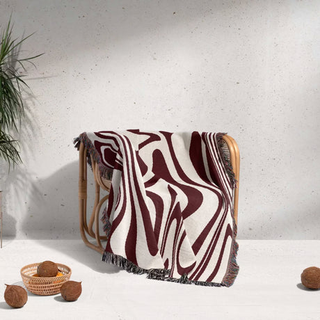 Red marble woven throw blanket for couch draped over a wooden chair against a white wall.