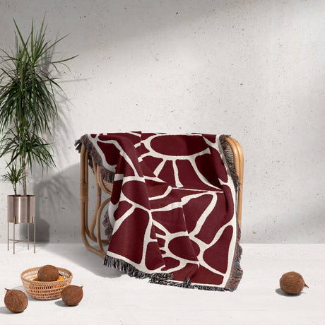 Red Matisse tapestry throw blanket for couch and chair draped over a chair with a plant and coconuts in the background.