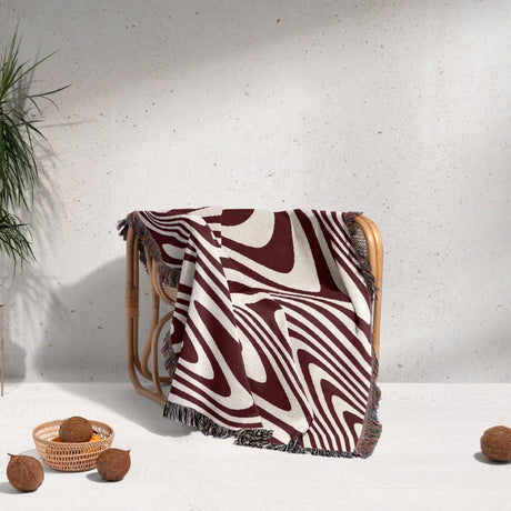 Red modern decorative woven throw blanket with abstract pattern draped over a chair against a light background