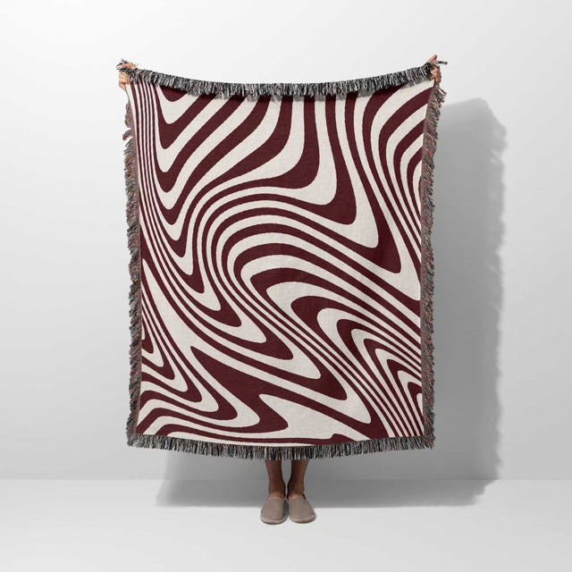 Red modern decorative woven throw blanket with a swirling pattern draped over a person on a white background