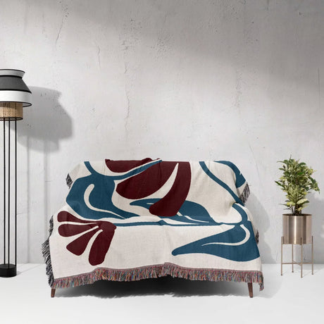 Decorative red and blue Matisse tapestry throw blanket with abstract design draped over a couch against a white wall.
