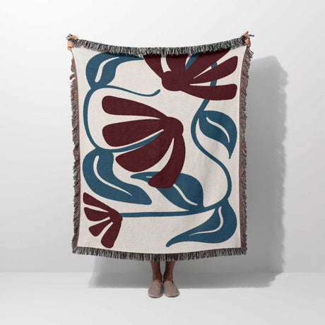 Person holding a red and blue Matisse tapestry throw blanket with floral pattern on a white background