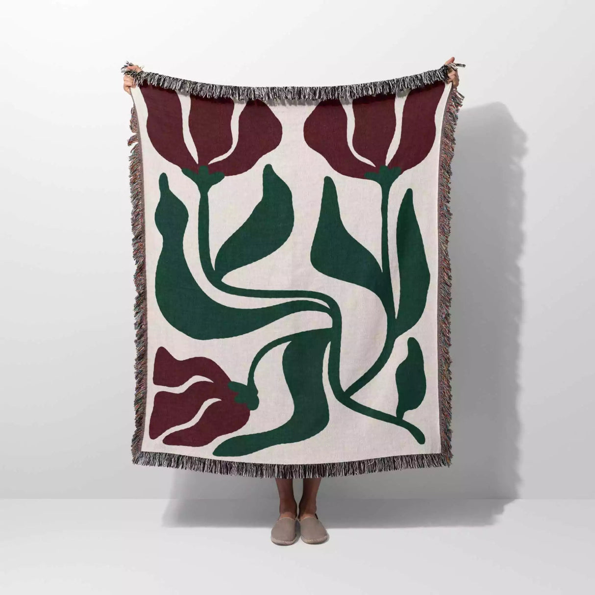Red and green Matisse flower woven throw blanket with floral pattern draped over a person on a white background