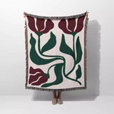 Red and green Matisse flower woven throw blanket with floral pattern draped over a person on a white background