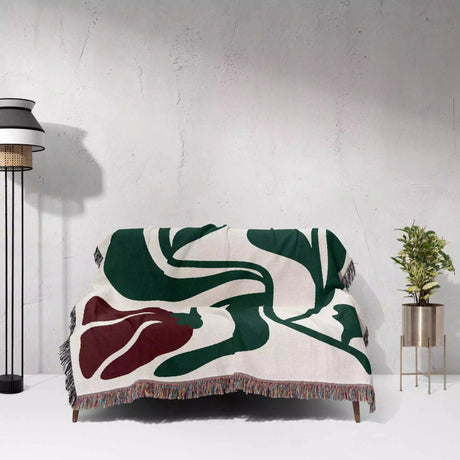 Red and green Matisse flower woven throw blanket abstract patterned blanket draped over a chair against a white wall.