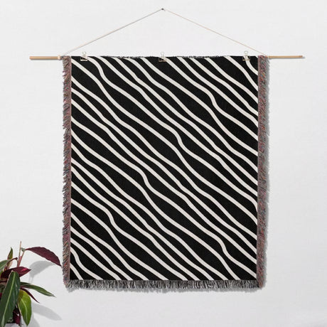 Black and white retro abstract art woven blanket throw tapestry with fringes hanging on a wooden rod against a white wall.