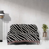 Black and white retro abstract art woven blanket throw tapestry draped over a couch against a white wall.