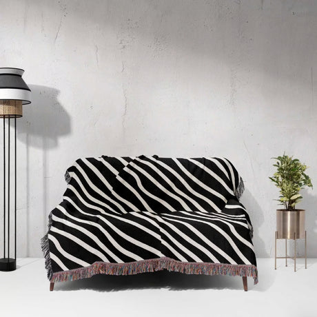 Black and white retro abstract art woven blanket throw tapestry draped over a couch against a white wall.