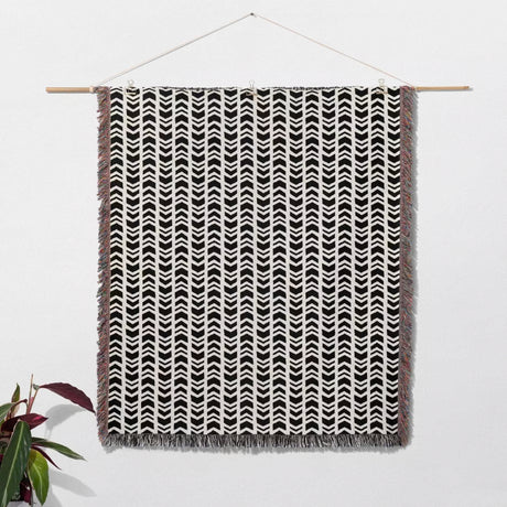 Black and white retro arrow lines woven blanket throw tapestry with fringe hanging on a wooden rod against a white wall.
