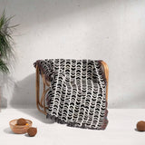 Black and white retro arrow lines woven blanket throw tapestry draped over a wooden chair on a light gray background