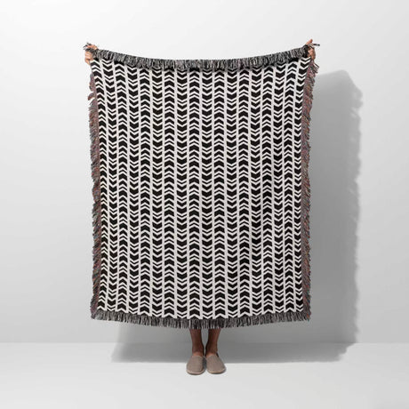 Person holding a black and white retro arrow lines woven blanket throw tapestry against a white background