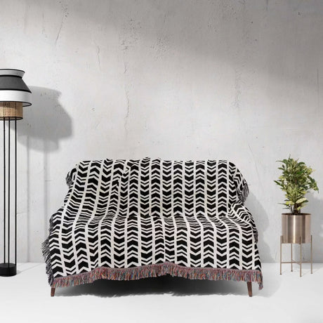 Black and white retro arrow lines woven blanket throw tapestry draped over a couch against a light gray wall.