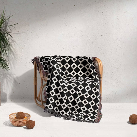 Black and white retro checker woven blanket throw tapestry draped over a wooden chair against a light gray wall.