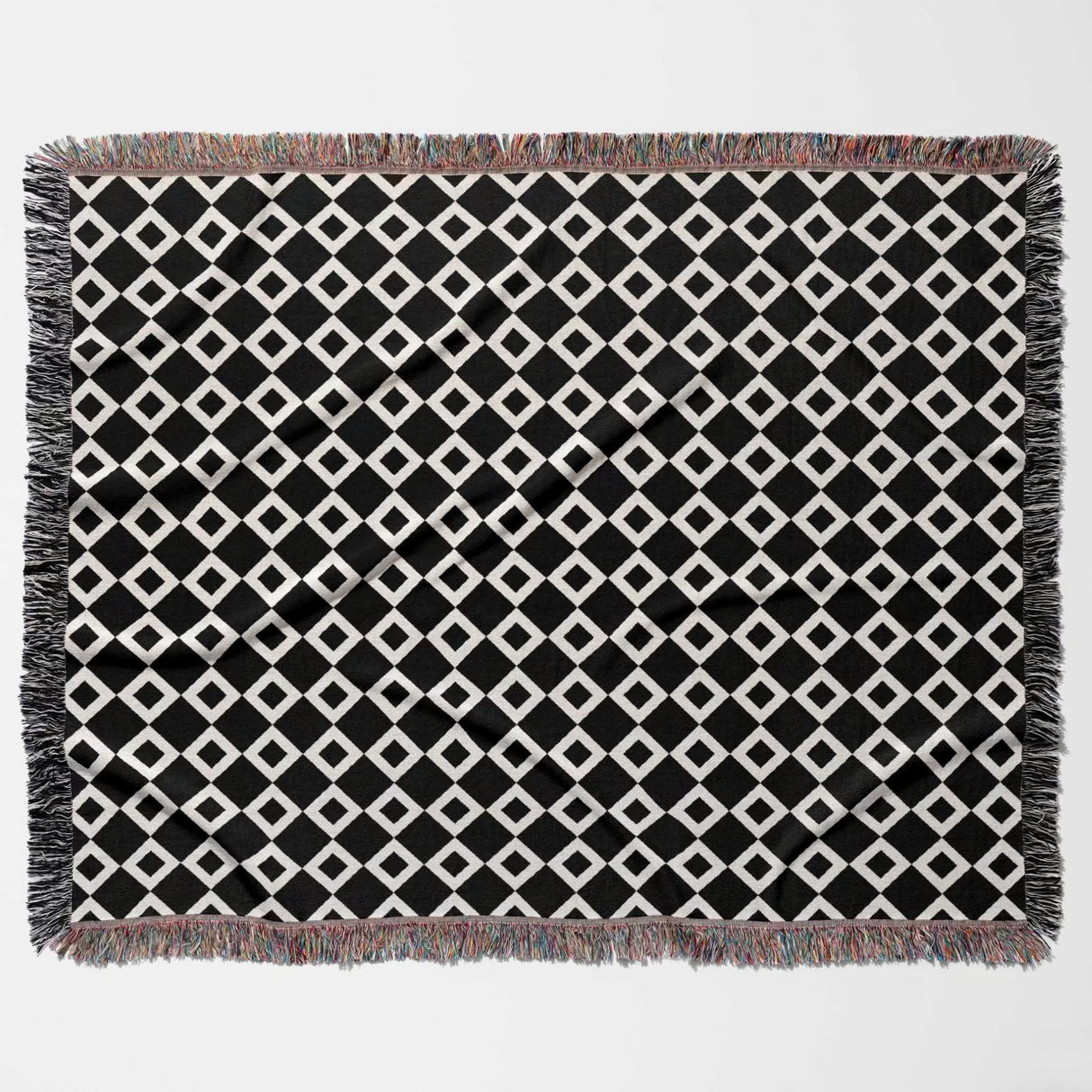 Black and white retro checker woven blanket throw tapestry with fringe flat lay on a light gray background