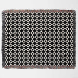 Black and white retro checker woven blanket throw tapestry with fringe flat lay on a light gray background
