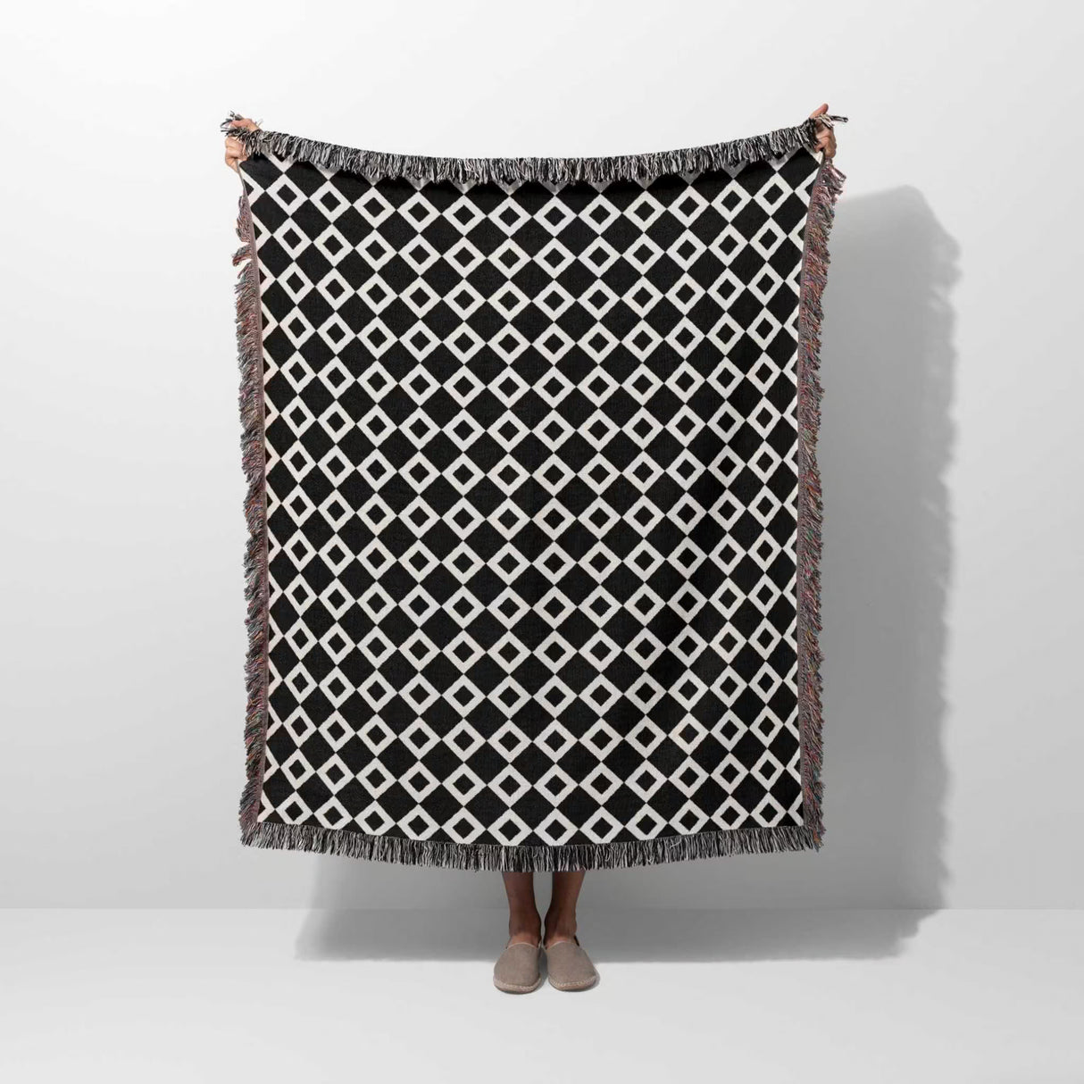 Black and white retro checker woven blanket throw tapestry with fringe held by a person on a white background