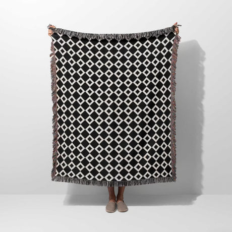 Black and white retro checker woven blanket throw tapestry with fringe held by a person on a white background