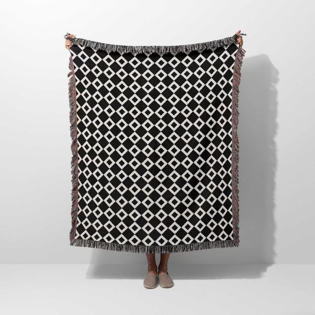 Black and white retro checker woven blanket throw tapestry with fringe held by a person on a white background