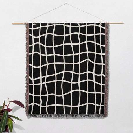 Black and white retro checkered woven blanket throw tapestry hanging on a wooden rod against a white wall.