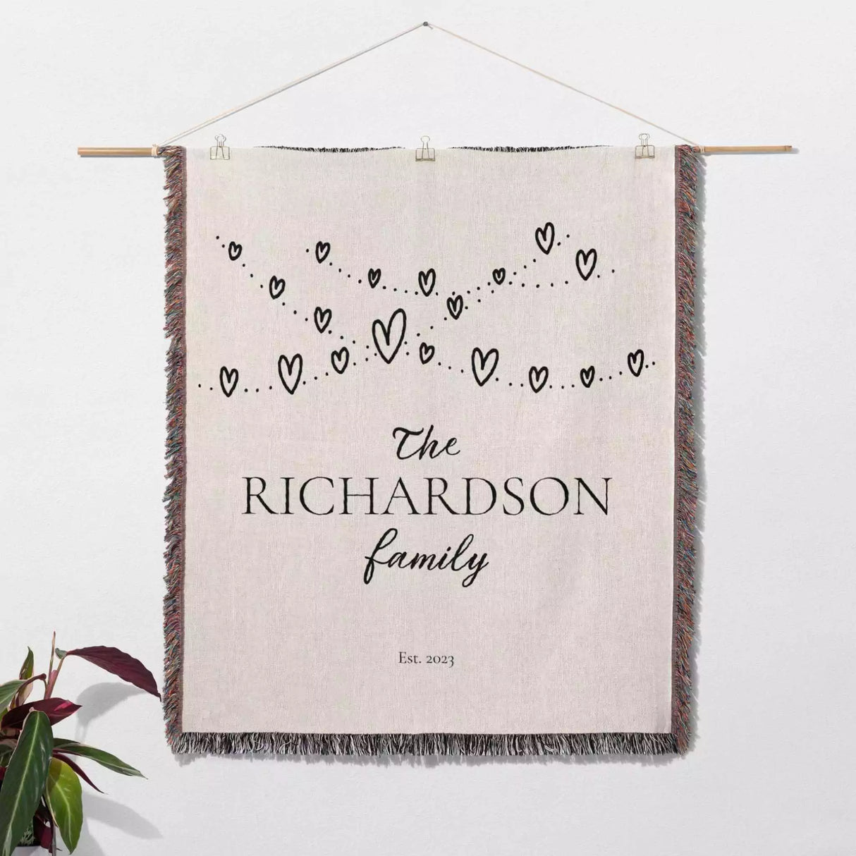 Romantic anniversary custom name blanket with 'The Richardson family' text and heart design hanging on a white wall.