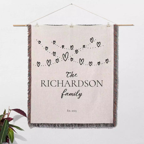 Romantic anniversary custom name blanket with 'The Richardson family' text and heart design hanging on a white wall.