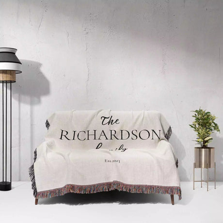 Romantic anniversary custom name blanket draped over a couch displaying 'The Richardson Family' on a white wall background.