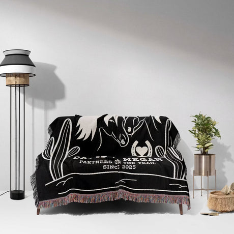 Romantic western 2nd anniversary gift - woven throw blanket with white designs and text draped over a couch in a room with a lamp and plant.