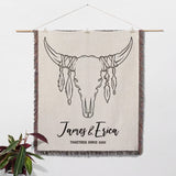 Rustic bull skull cotton anniversary gift woven throw blanket with bull skull design and 'James & Erica Together Since 2022' text, hanging on a white wall.