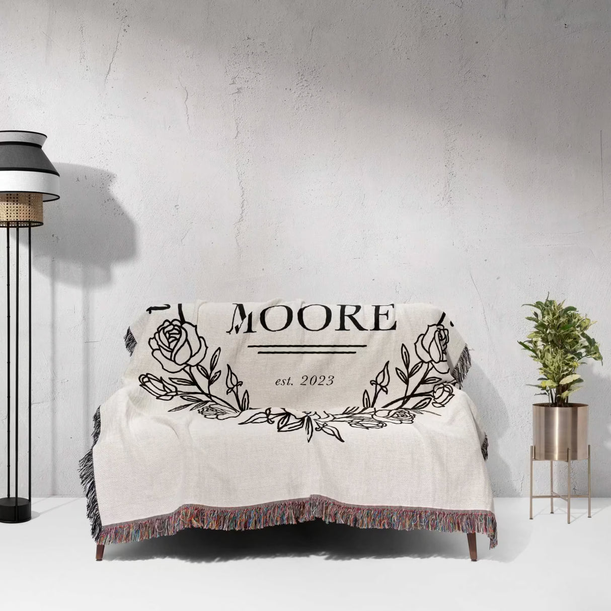 Rustic Mr and Mrs 2nd year anniversary gift woven throw blanket with 'MOORE est. 2023' design on a couch against a gra wall.