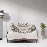 Rustic Mr and Mrs 2nd year anniversary gift woven throw blanket with 'MOORE est. 2023' design on a couch against a gra wall.