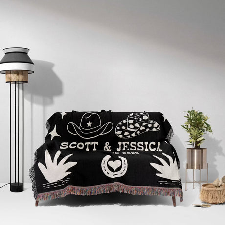 Rustic western 2nd anniversary gift woven throw blanket with white designs and text on a sofa in a room with a lamp and plant.