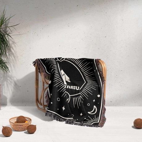 The Sagittarius Zodiac blanket is casually draped over a wooden chair, demonstrating its texture and drape. The intricate arrow symbol and celestial design are partially visible, adding a decorative touch to the setting.