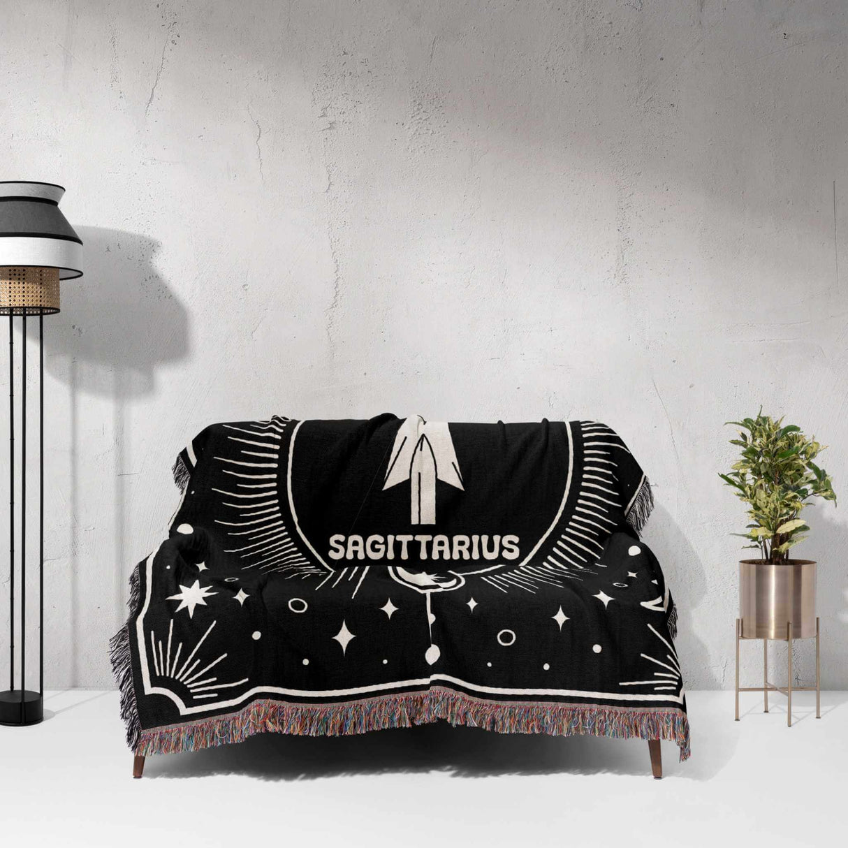 The blanket is spread out over a couch, revealing the full Sagittarius design in black and white. The image shows the blanket's size and how it complements a living room setting, with the celestial design adding a stylish accent.