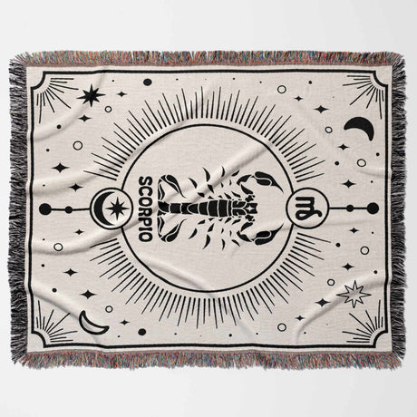 A horizontal flat lay of the Scorpio Zodiac Blanket, depicting the detailed Scorpio symbol in black against an off-white background. The multicolored fringe adds a vibrant touch, making it a stunning piece for home decor or as a thoughtful birthday gift.