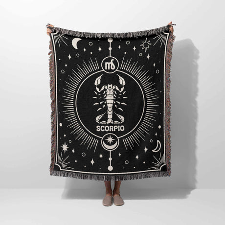 A person holding the Scorpio Zodiac Blanket upright, displaying its full design. The intricate Scorpio symbol and celestial patterns are clearly visible, along with the multicolor fringe, illustrating the blanket's size and design.