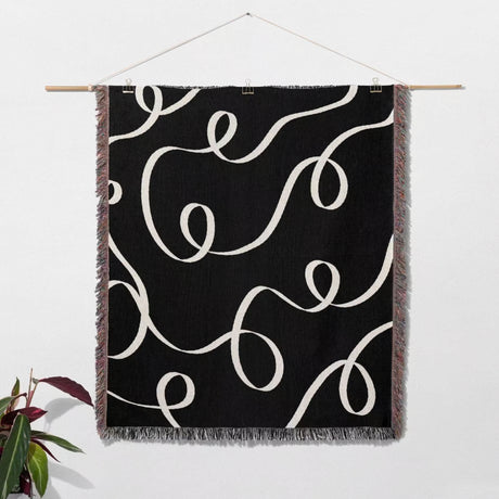 Black and white scribble lined woven blanket throw with fringe hanging on a white wall.