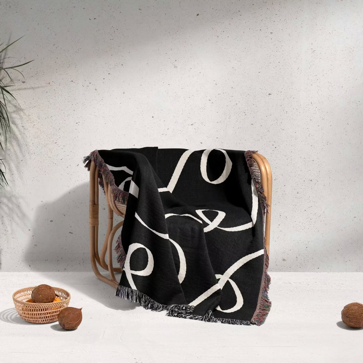 Black and white scribble lined woven blanket throw with fringe draped over a chair against a light gray background