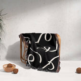 Black and white scribble lined woven blanket throw with fringe draped over a chair against a light gray background