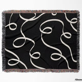 Black and white scribble lined woven blanket throw with fringe flat lay on a plain background.